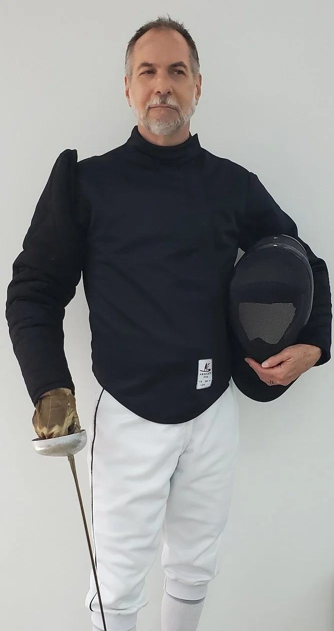 Head coach Robert Szokolay in fencing jacket holding an épée and mask